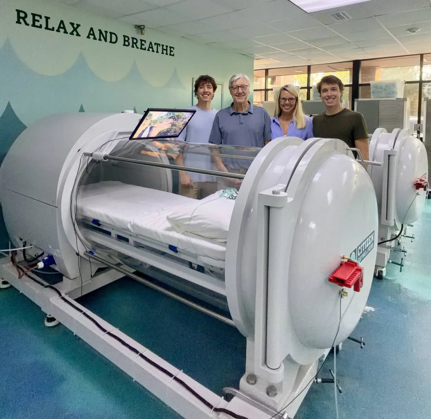 The Citizen OxyWellness family standing behind one of the clinic’s hyperbaric oxygen chambers in Dothan, AL
